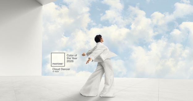 A person dressed in flowing white stands with arms outstretched against a sky of soft clouds, representing Pantone Color of the Year 2026, Cloud Dancer.