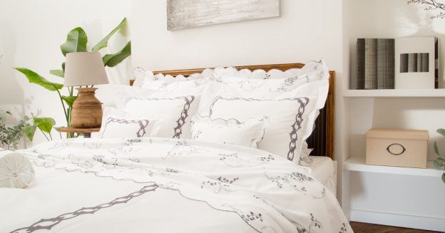 White luxury bedding with embroidered chain border and floral details styled on a bed with layered pillows and duvet in a serene, elegant bedroom